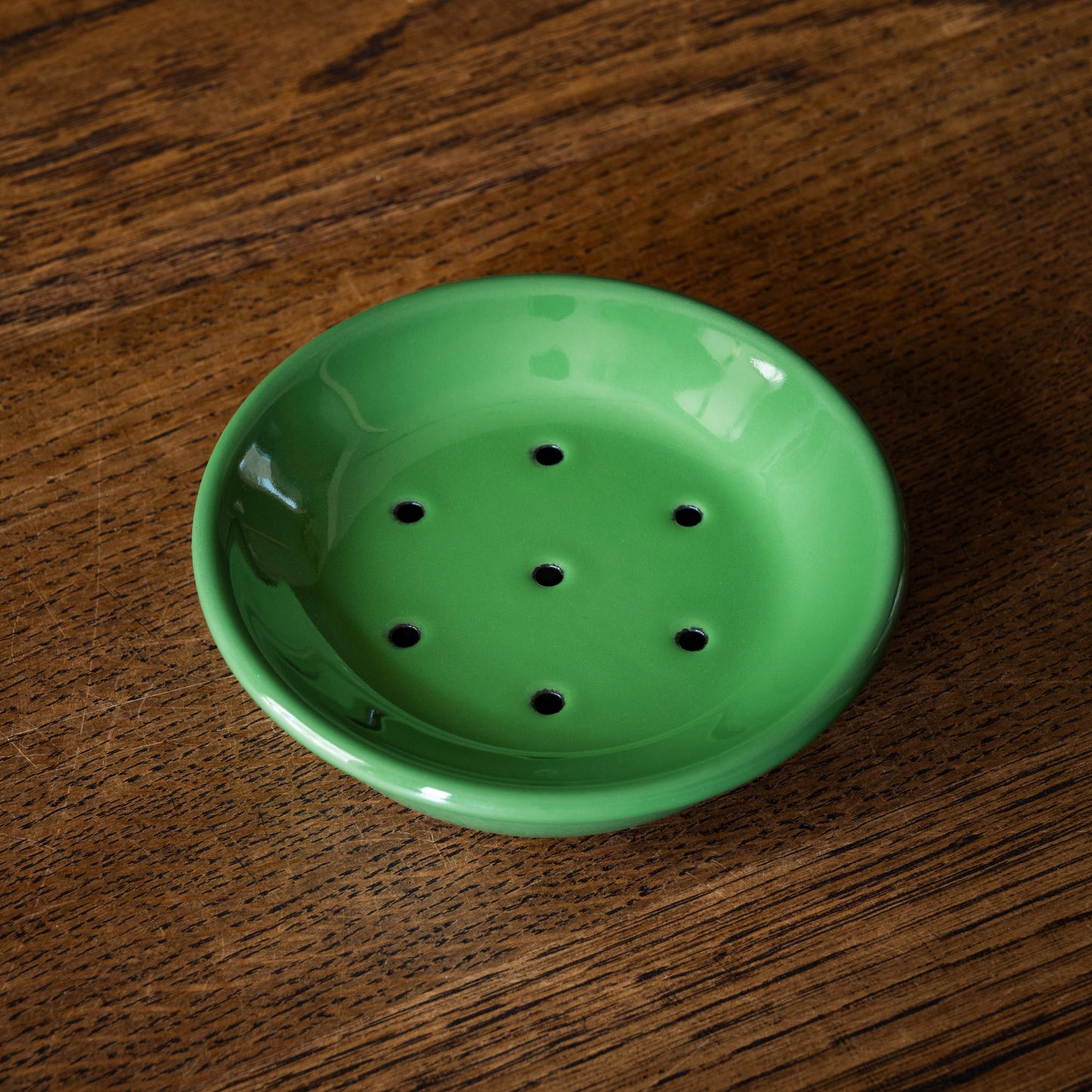 Green enamel soap dish with draining holes on a wooden surface