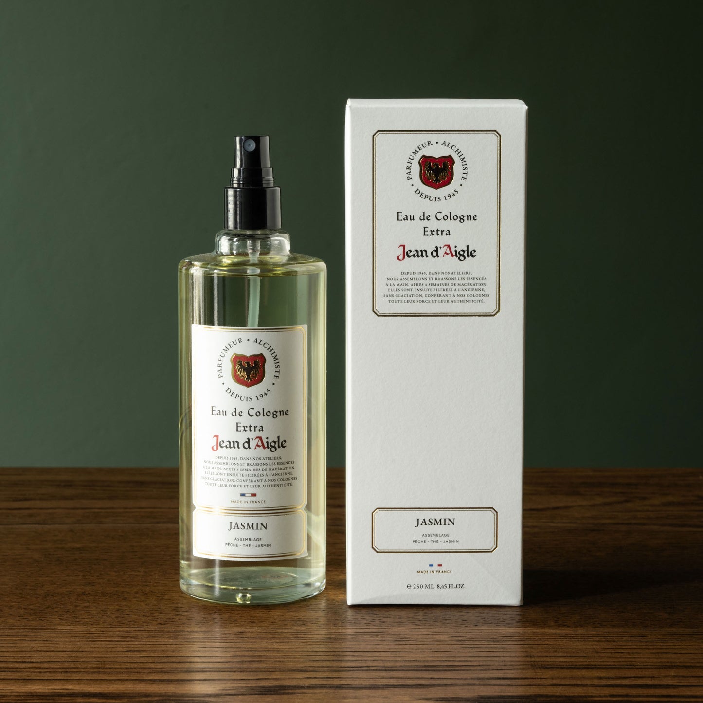 Bottle and box of Jean d'Aigle Jasin cologne on a wooden surface with a dark green background