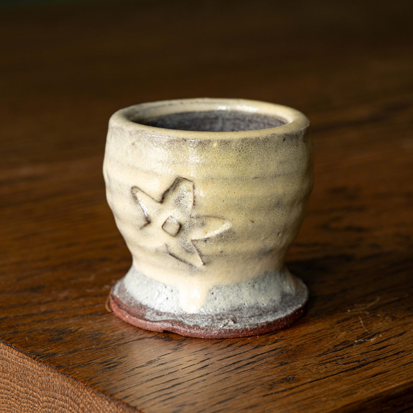 Joshua Williams cream earthenware egg cup with a floral design on a wooden surface
