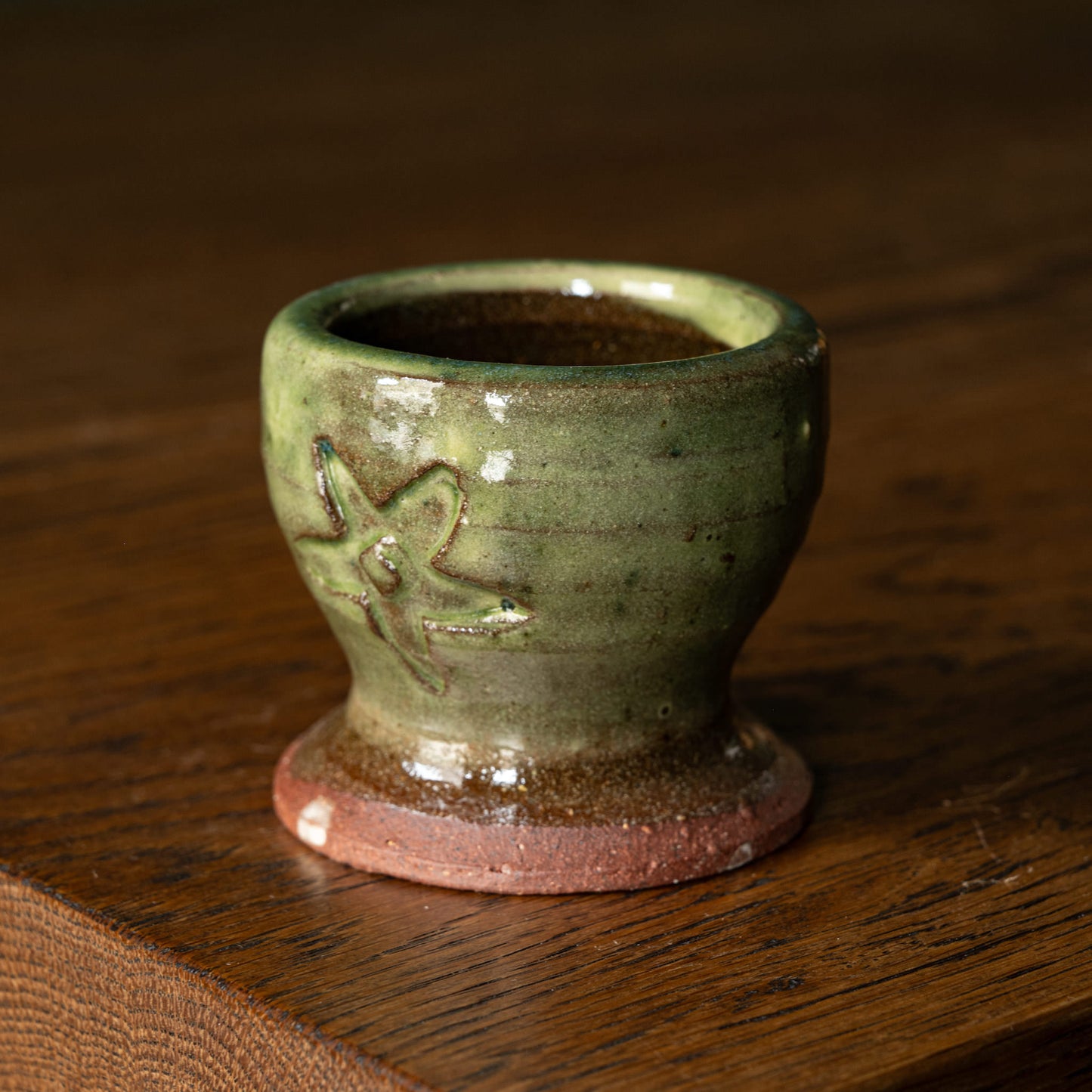 Joshua Williams green earthenware egg cup with a floral design on a wooden surface