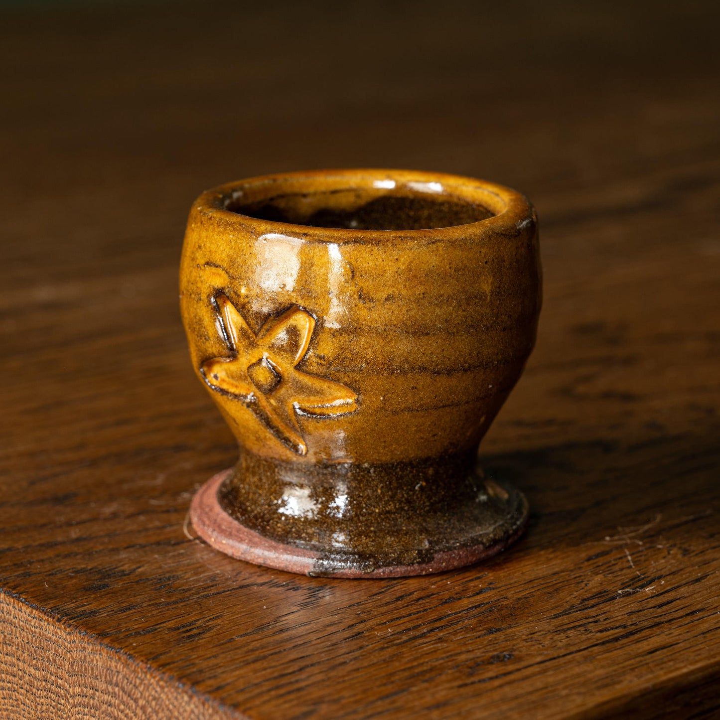 Joshua Williams ochre earthenware egg cup with floral design on a wooden surface