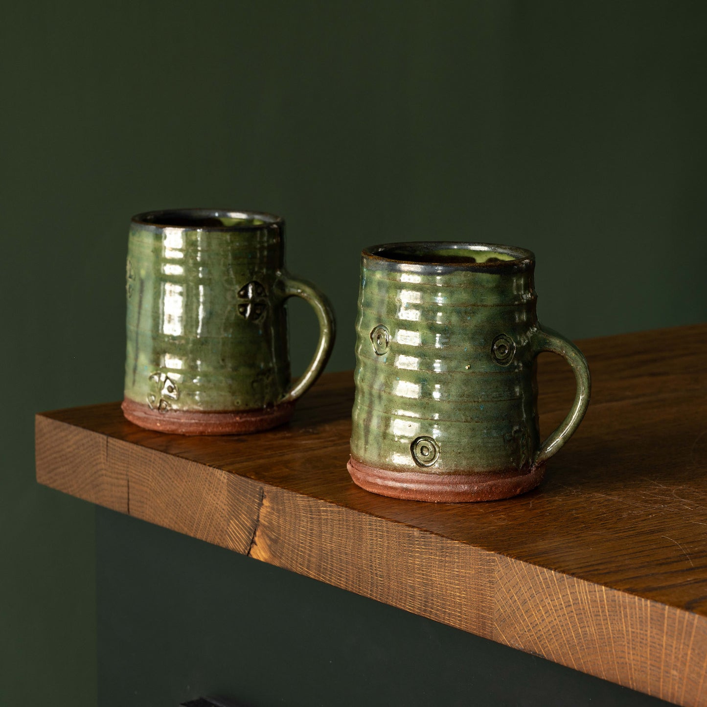 Two Joshua Williams green earthenware mugs on a wooden shelf