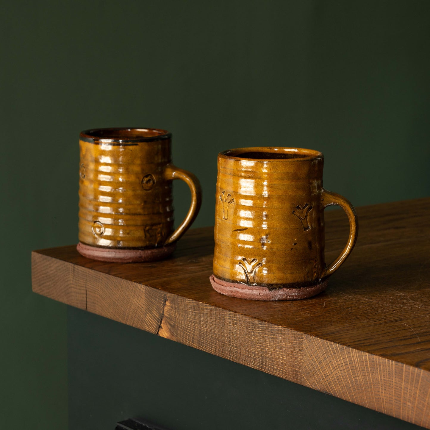 Two Joshua Williams ochre earthenware mugs on a wooden shelf
