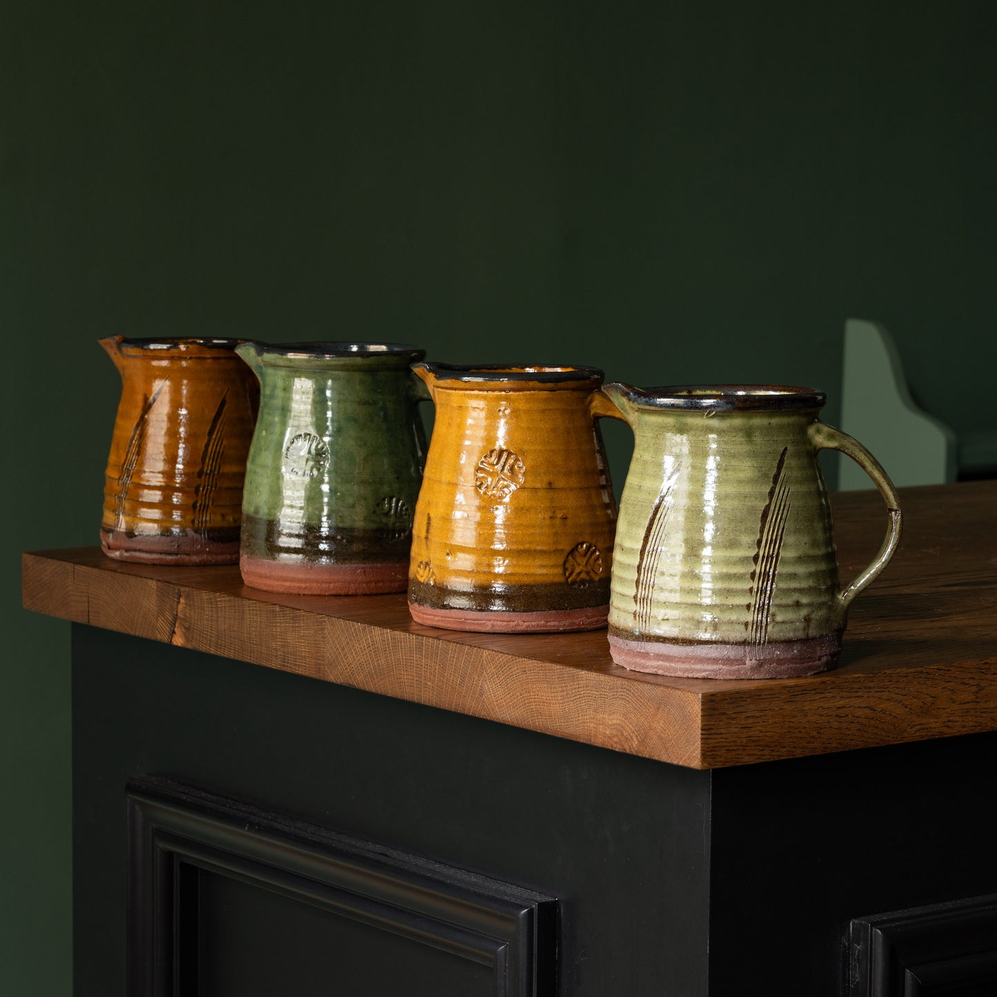 Joshua Williams earthenware jugs in different colours on a wooden surface with a dark background