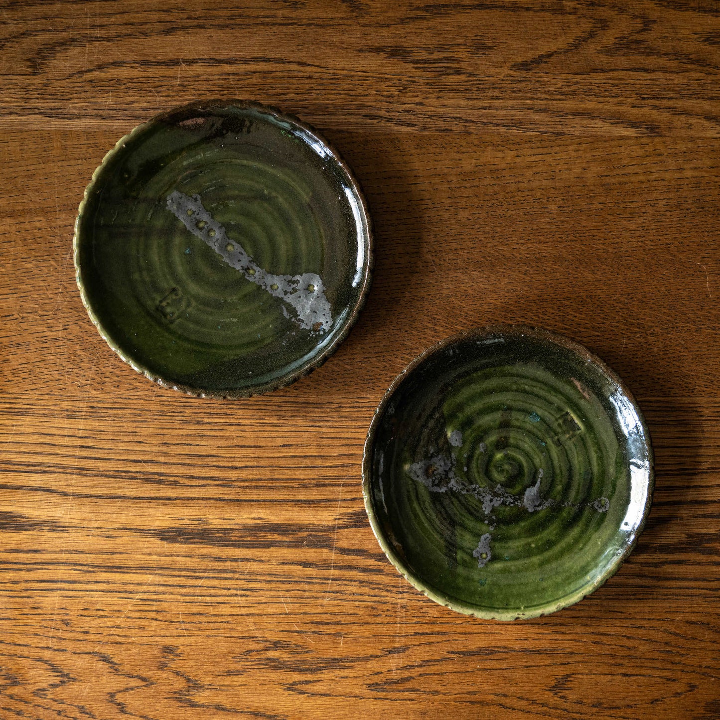 Two Joshua Williams earthenware plates with unique slip designs with a green base glaze on a wooden surface