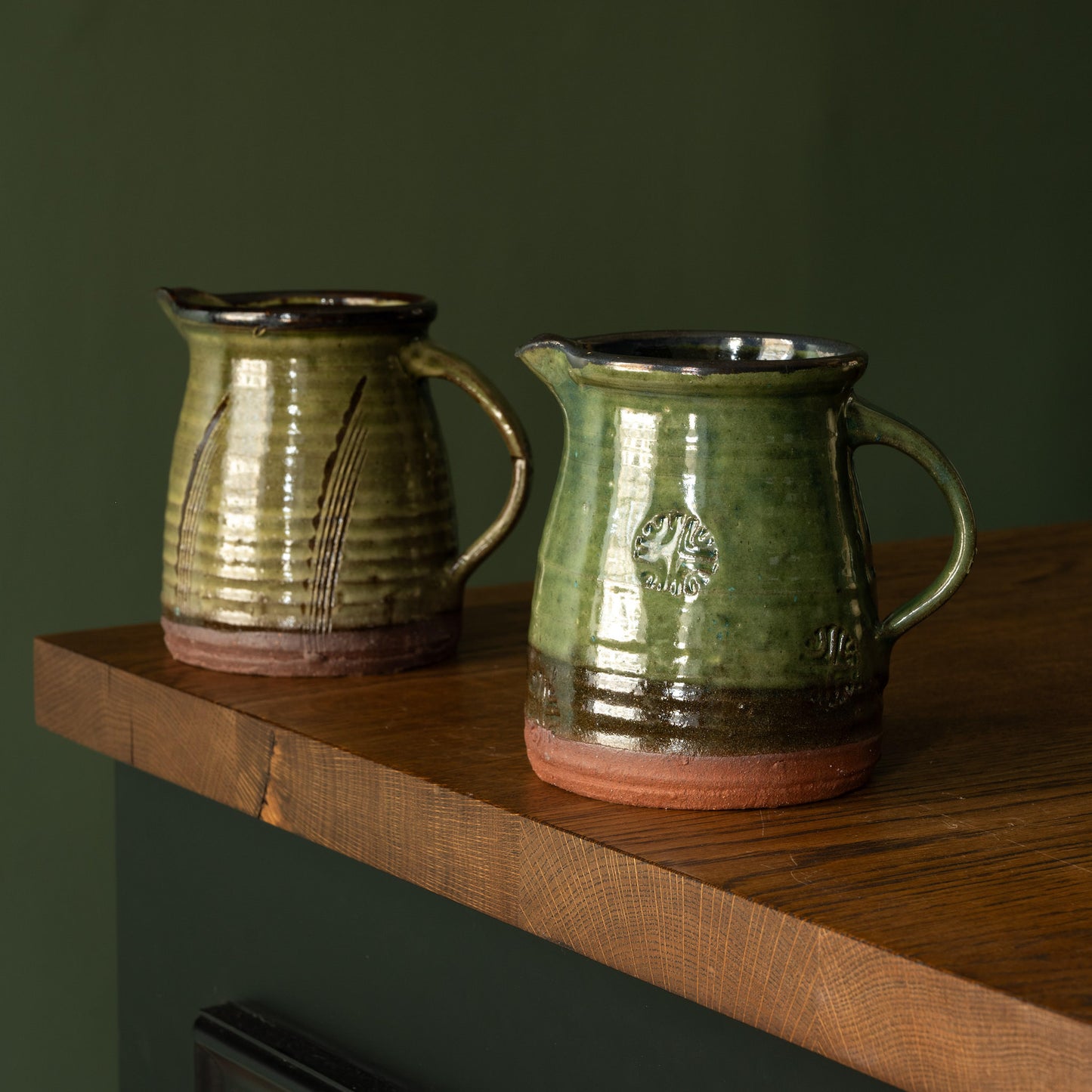 Two Joshua Williams green earthenware pitchers on a wooden shelf