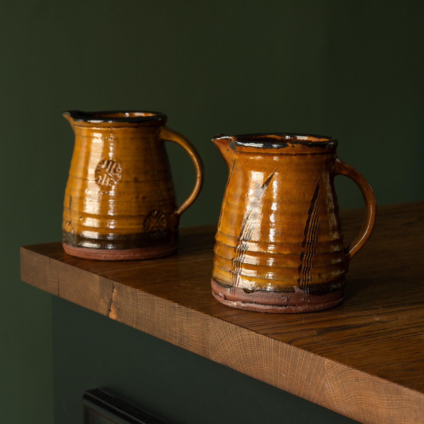 Two Joshua Williams ochre earthenware jugs on a wooden shelf