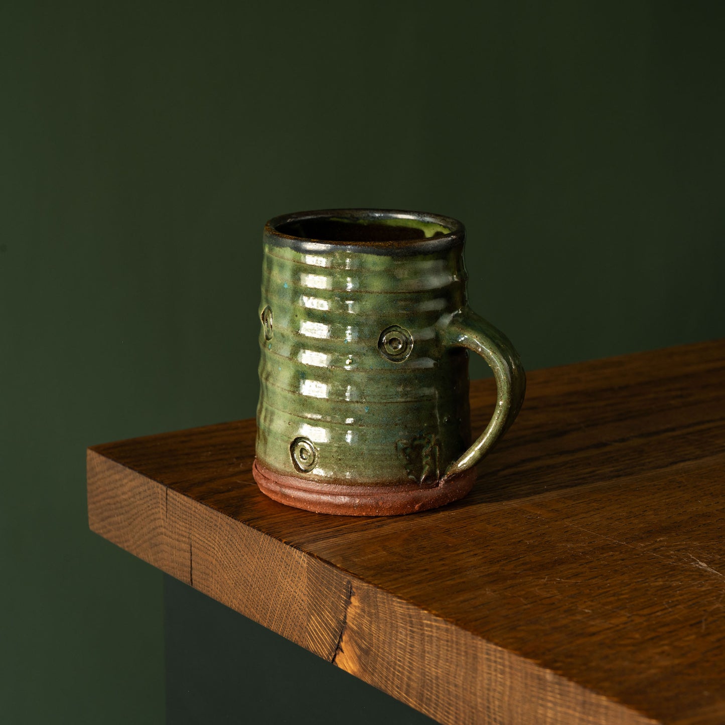 Green Joshua Williams earthenware mug on a wooden shelf