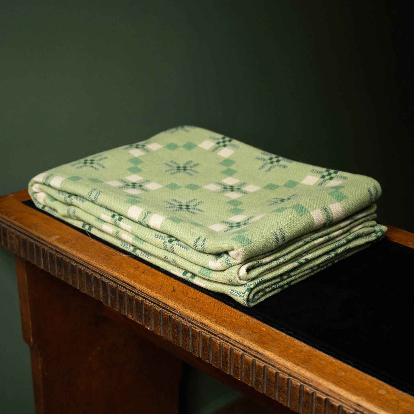 Melin Tregwynt St Davids Cross Welsh Blanket in Deilen colourway folded on a desk.