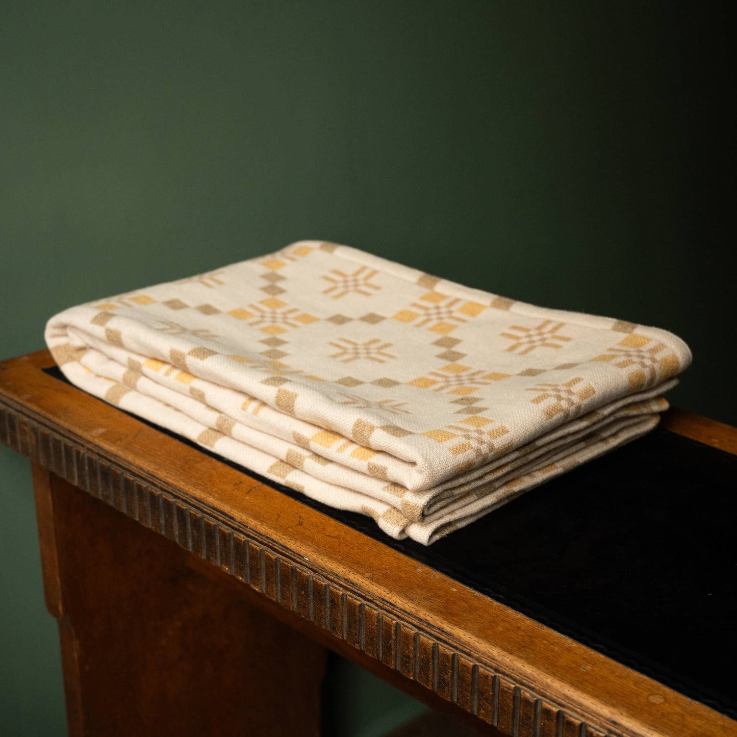 Melin Tregwynt St Davids Cross Welsh Blanket in Traeth colourway folded on desk.