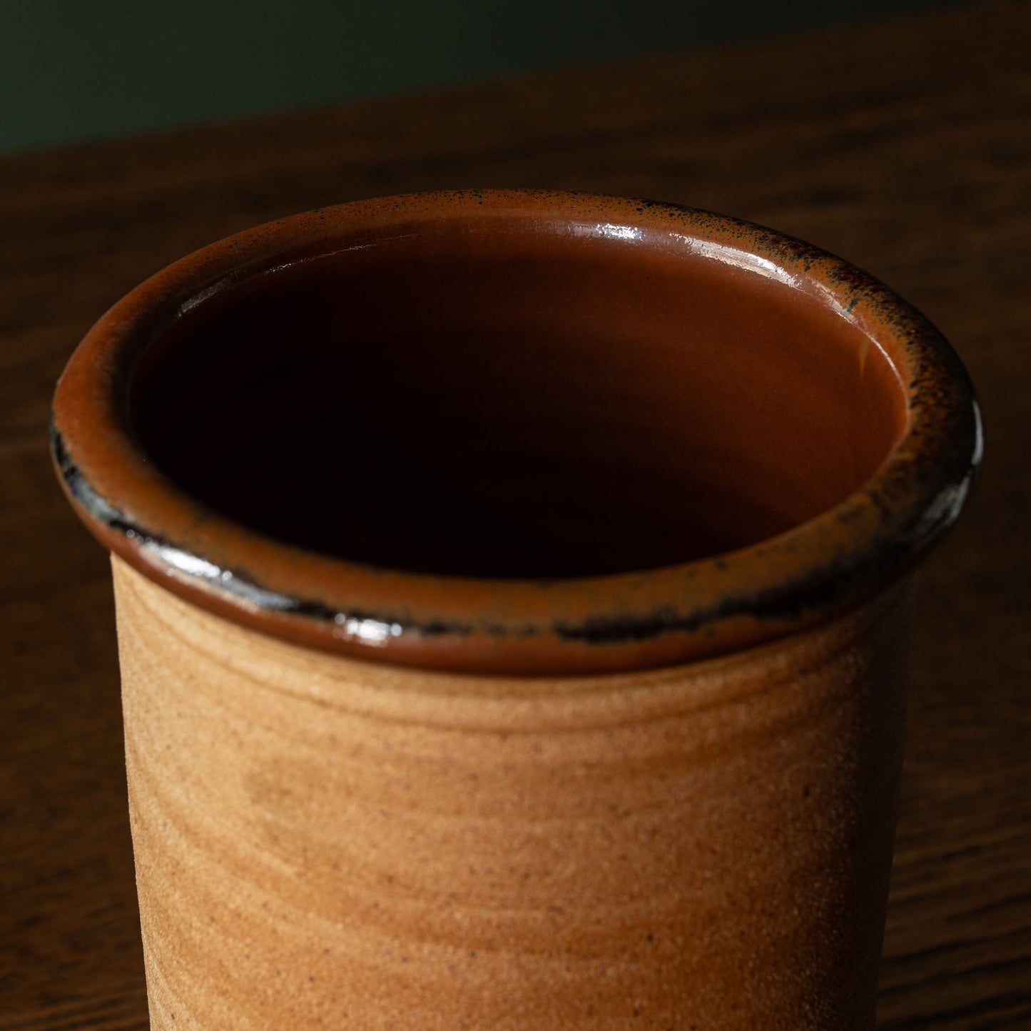 Close-up of Muchelney Pottery ceramic utensils tidy with a warm terracotta brown interior and rim, set against a dark wooden background.