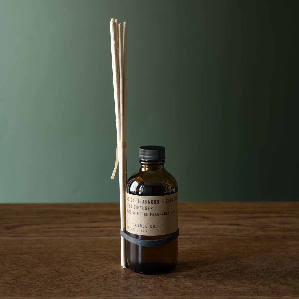 PF Candle Co amber glass reed diffuser bottle with a black cap a set of rattan diffuser sticks tied to the bottle.