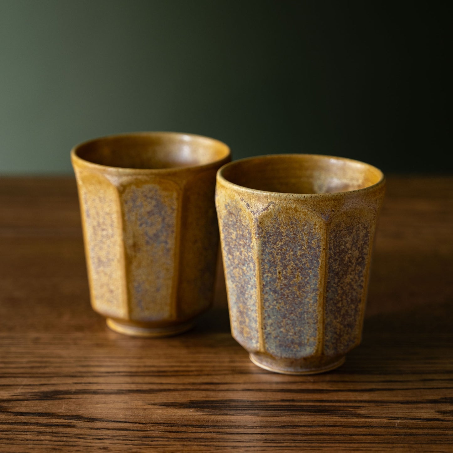 A pair of Pottery West ochre faceted beakers on a wooden table