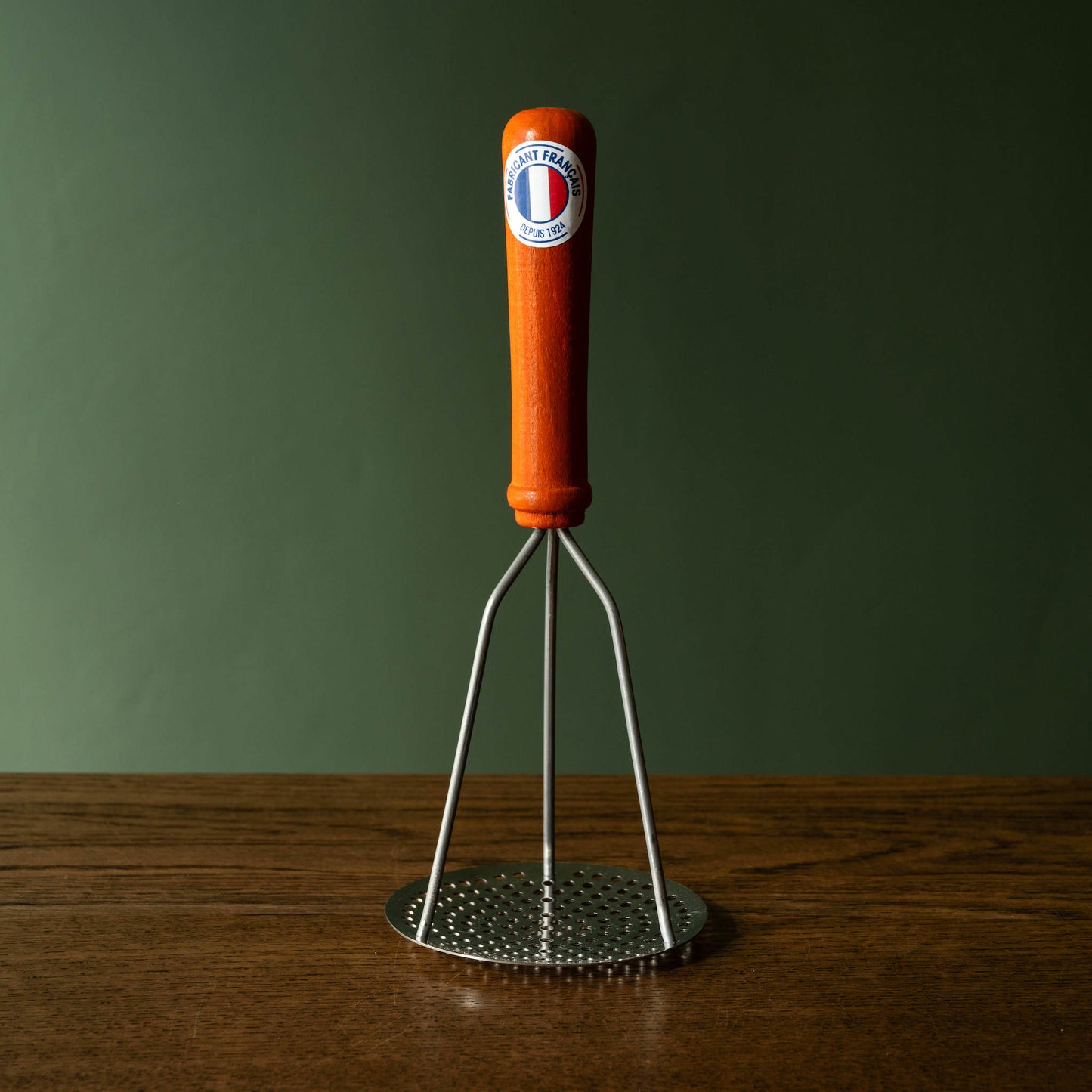 Potato masher with orange stained wood handle and steel masher