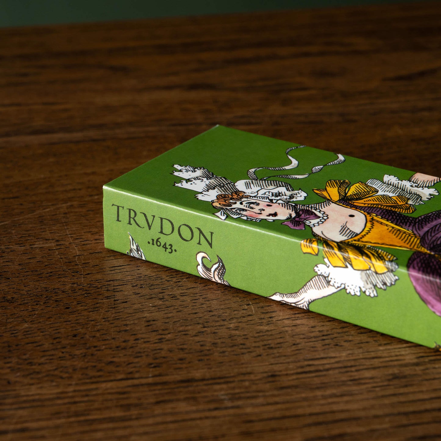 Close up of Trudon matches in a decorative box with a vintage-style illustration of a woman in a yellow and purple dress on a green background.