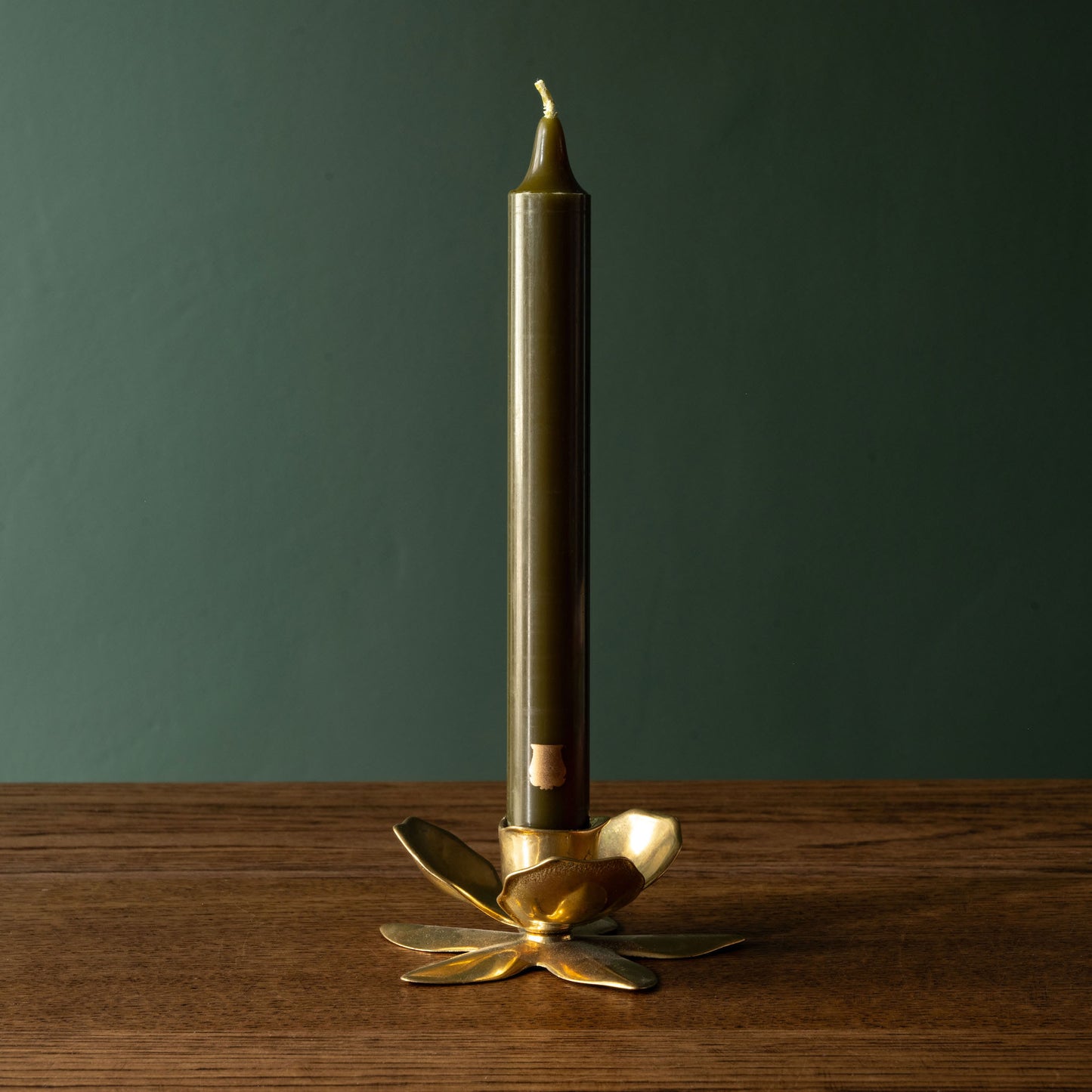 Trudon gold Flower Candle Holder with a khaki Madeleine taper candle on a wooden surface against a green background