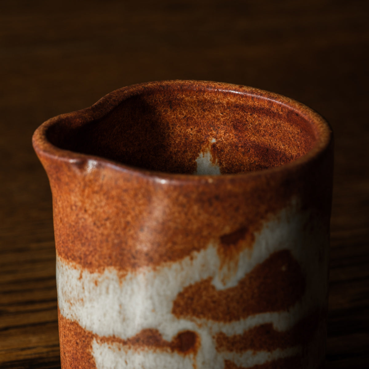 Close-up of Carrick Ceramics handmade small ceramic pitcher with a rustic brown and white glaze, set against a dark wooden background.