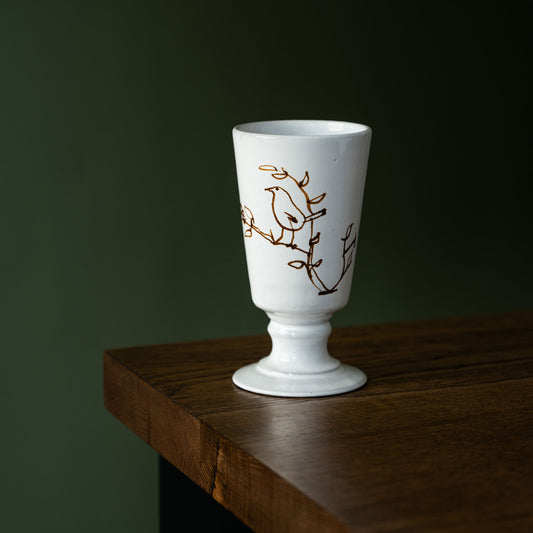 Carron Paris white ceramic footed vase with a bird illustration on a wooden surface against a dark background