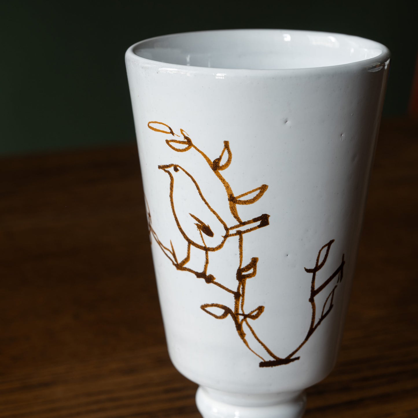 Close up of Carron Paris white ceramic L'oiseau footed vase with brown bird in a tree design on a wooden surface
