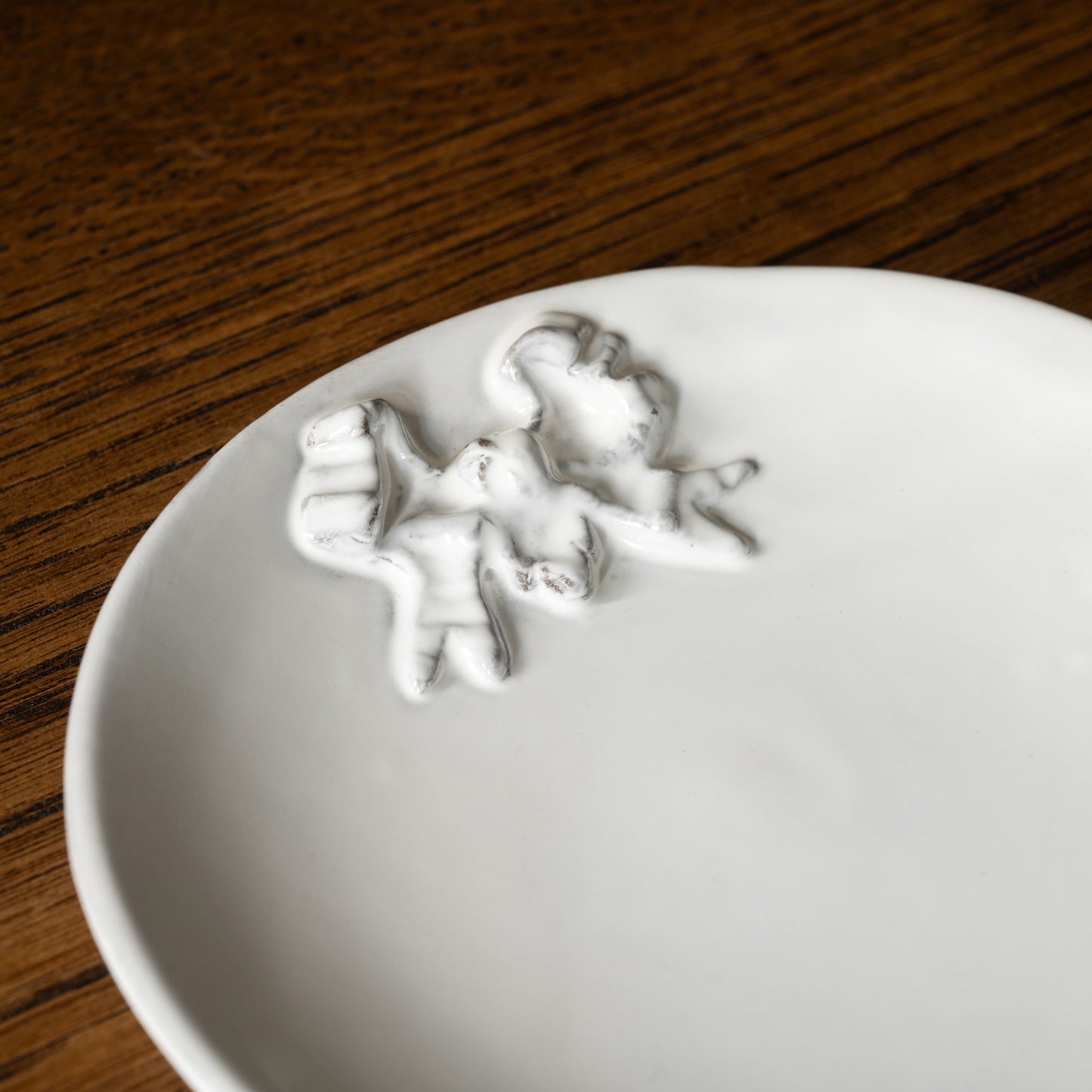 Close up of Carron Paris white Marie-Antoinette ceramic plate with a decorative ribbon design on a wooden surface
