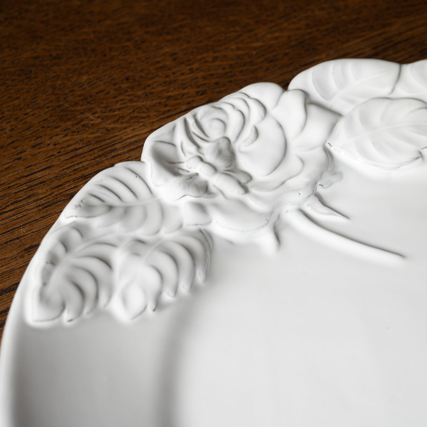 Close up of Carron Paris white ceramic decorative plate with rose floral pattern with a bee on a wooden surface