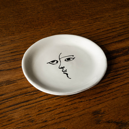 Carron Paris Toi et moi small plate in milky white glaze with an illustrated face design by Pierre Carron. 