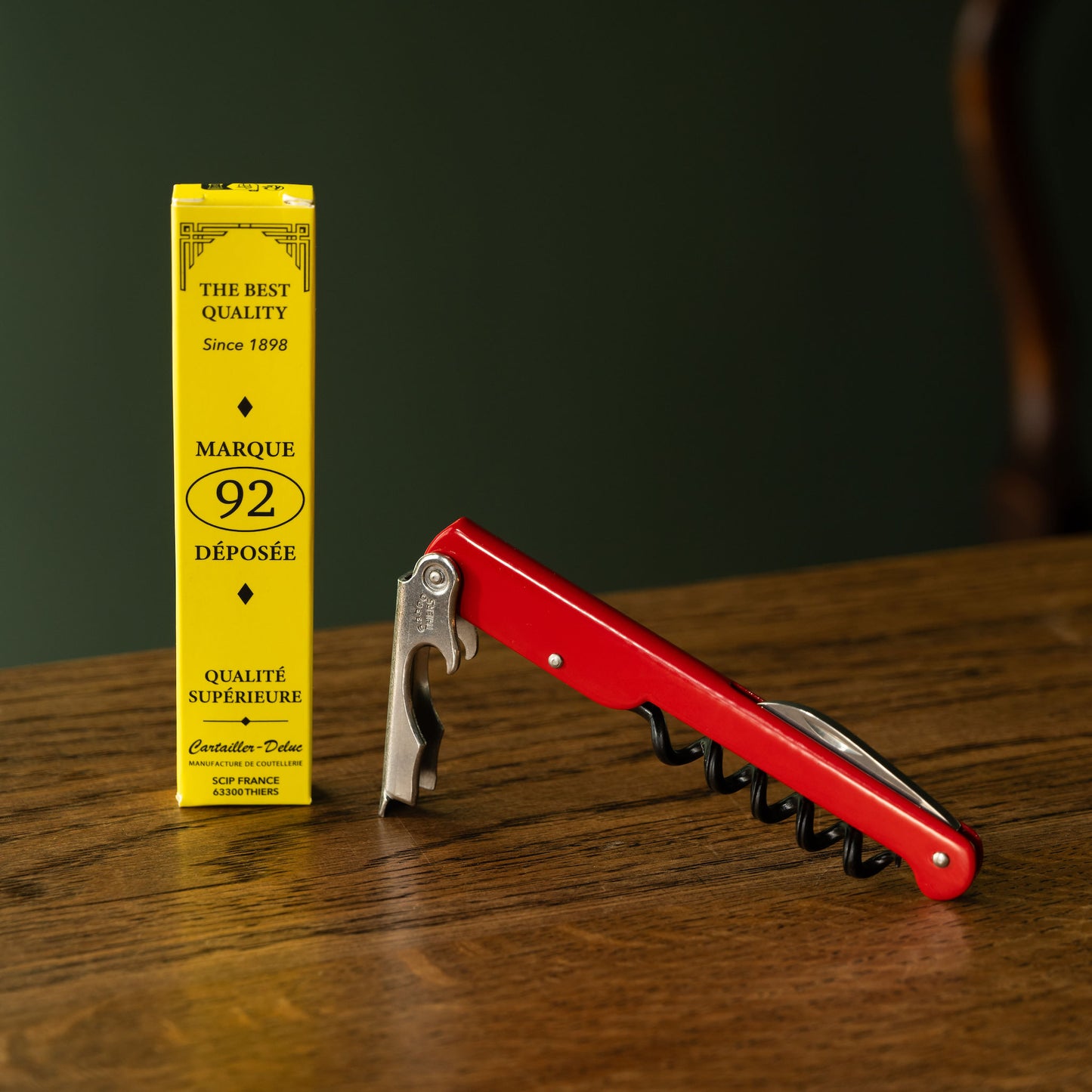 Red corkscrew next to a yellow box on a wooden surface with a dark background