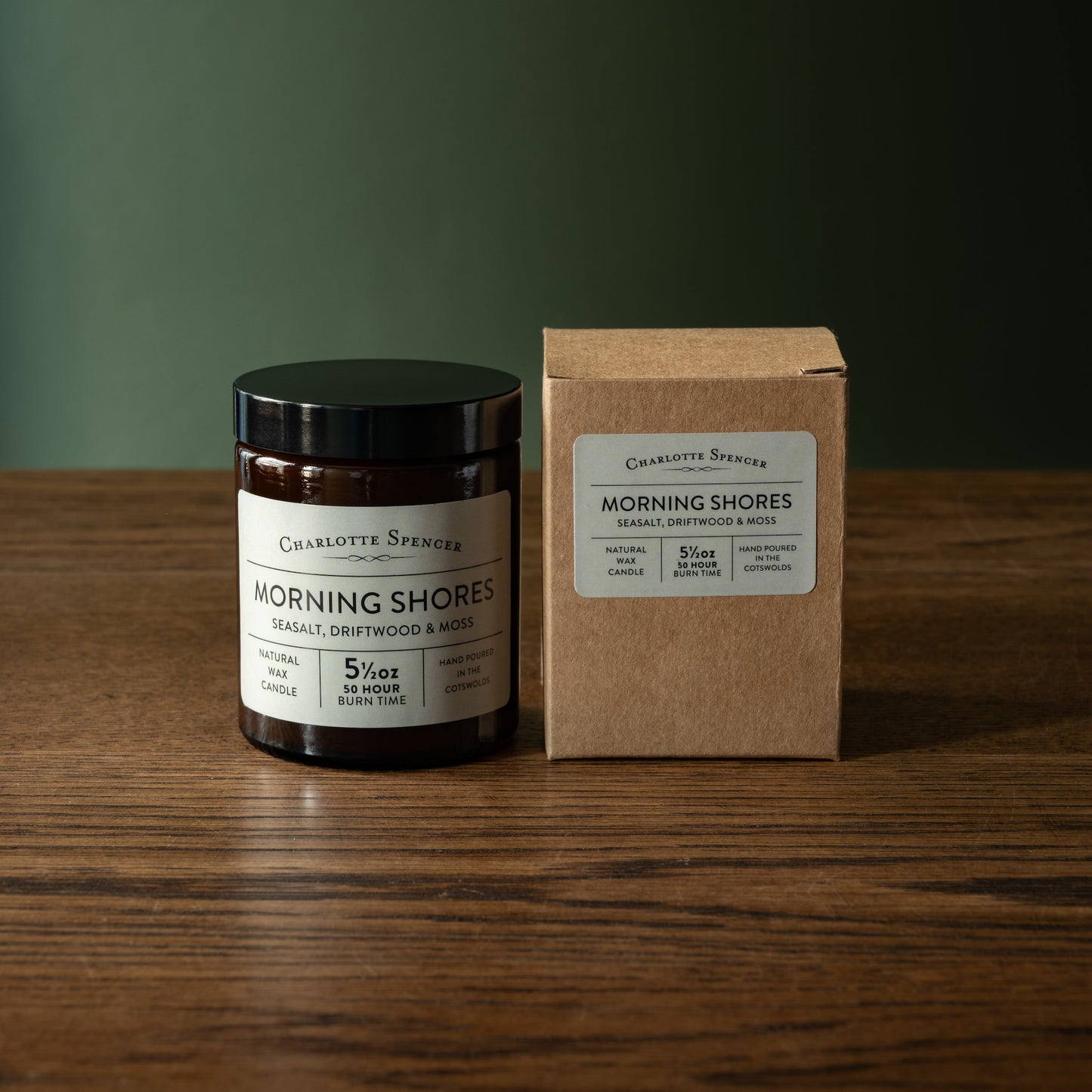Apothecary jar style candle and box of Charlotte Spencer 'Morning Shores' fragrance on a wooden surface with a green background