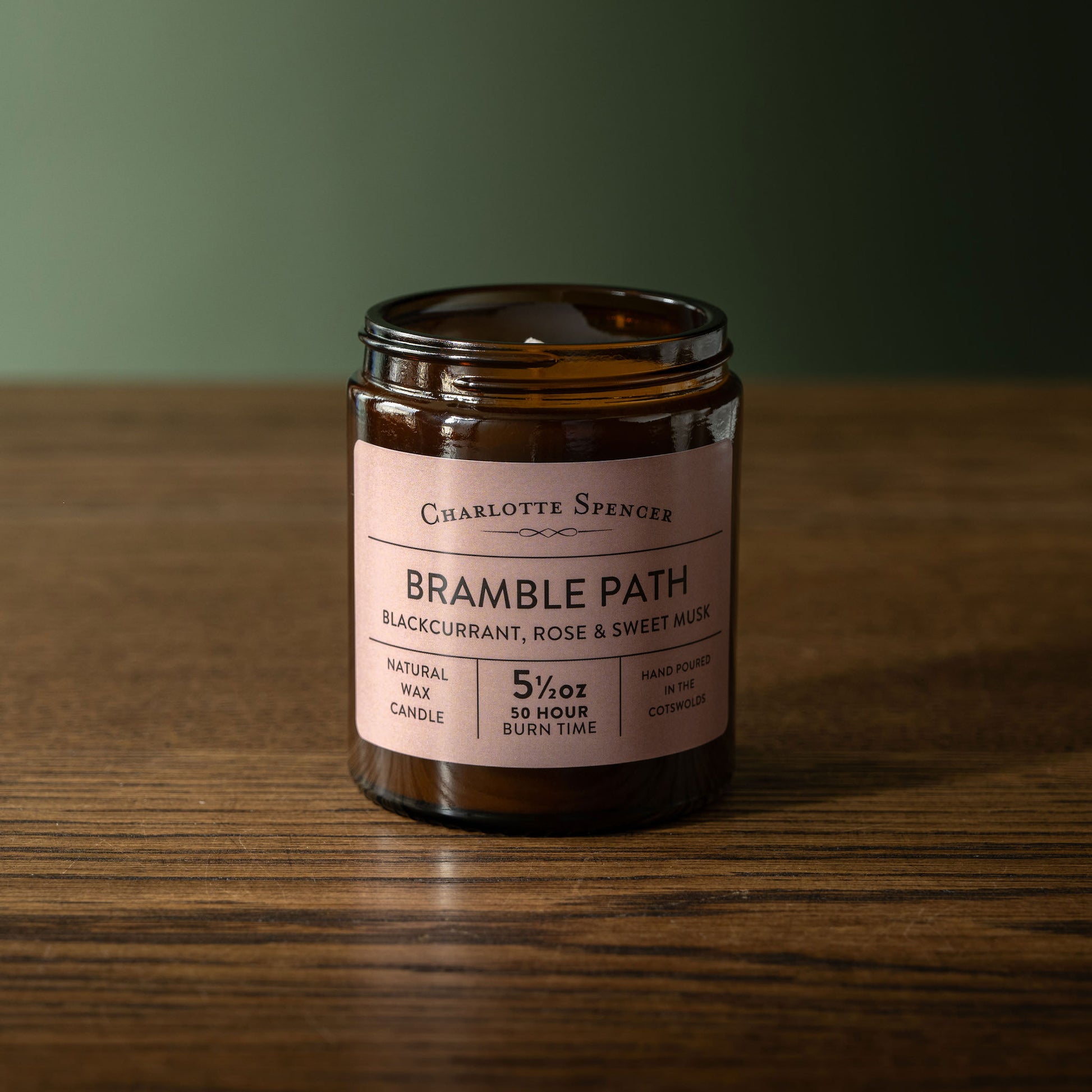 Charlotte Spencer 'Bramble Path' candle on a wooden surface with a green background