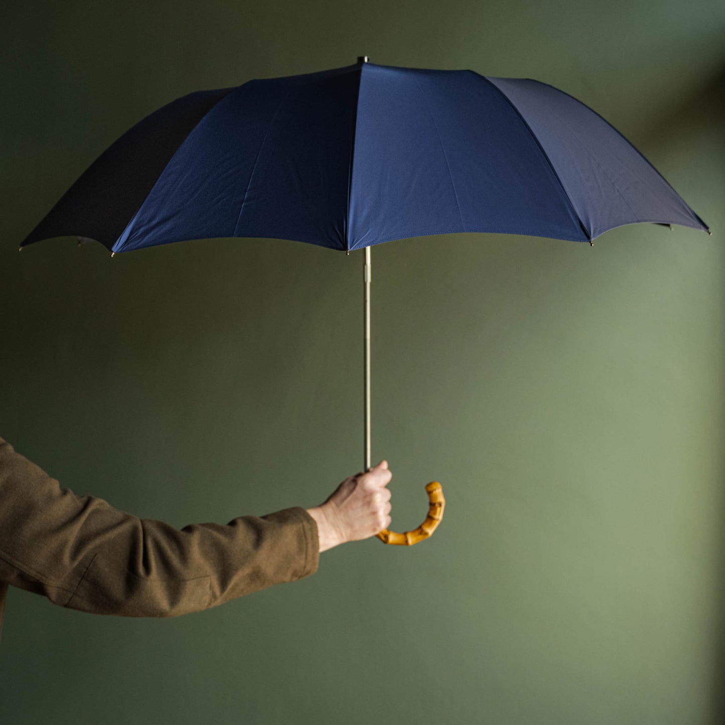 Person holding a Fox Umbrellas telescopic blue umbrella with a bamboo handle against a green background