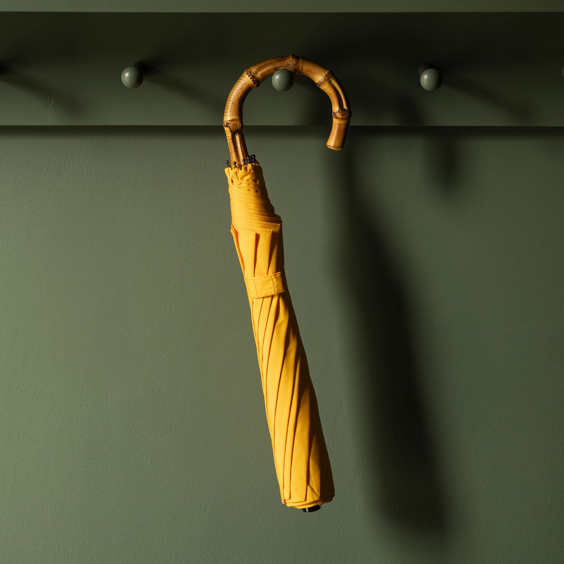 Yellow Fox Umbrellas telescopic umbrella with a bamboo handle against a dark green peg rail.