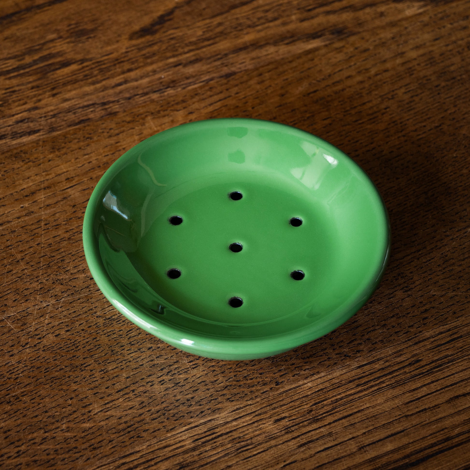 Green enamel soap dish with draining holes on a wooden surface