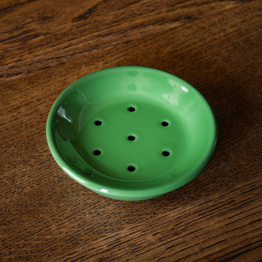 Green enamel soap dish with draining holes on a wooden surface