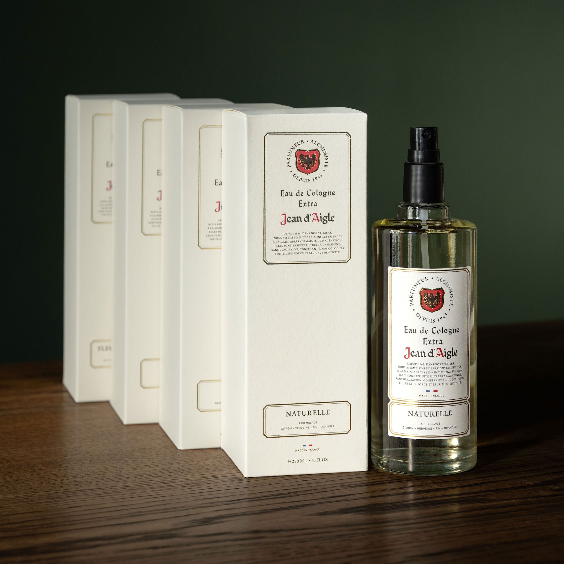 Bottle and boxes of Jean d'Aigle Eau de Cologne on a wooden surface with a dark background