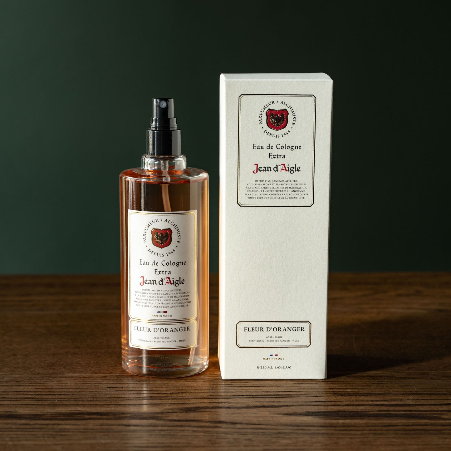 Bottle and box of Jean d'Aigle Fleur D'Oranger Eau de Cologne on a wooden surface with a dark background