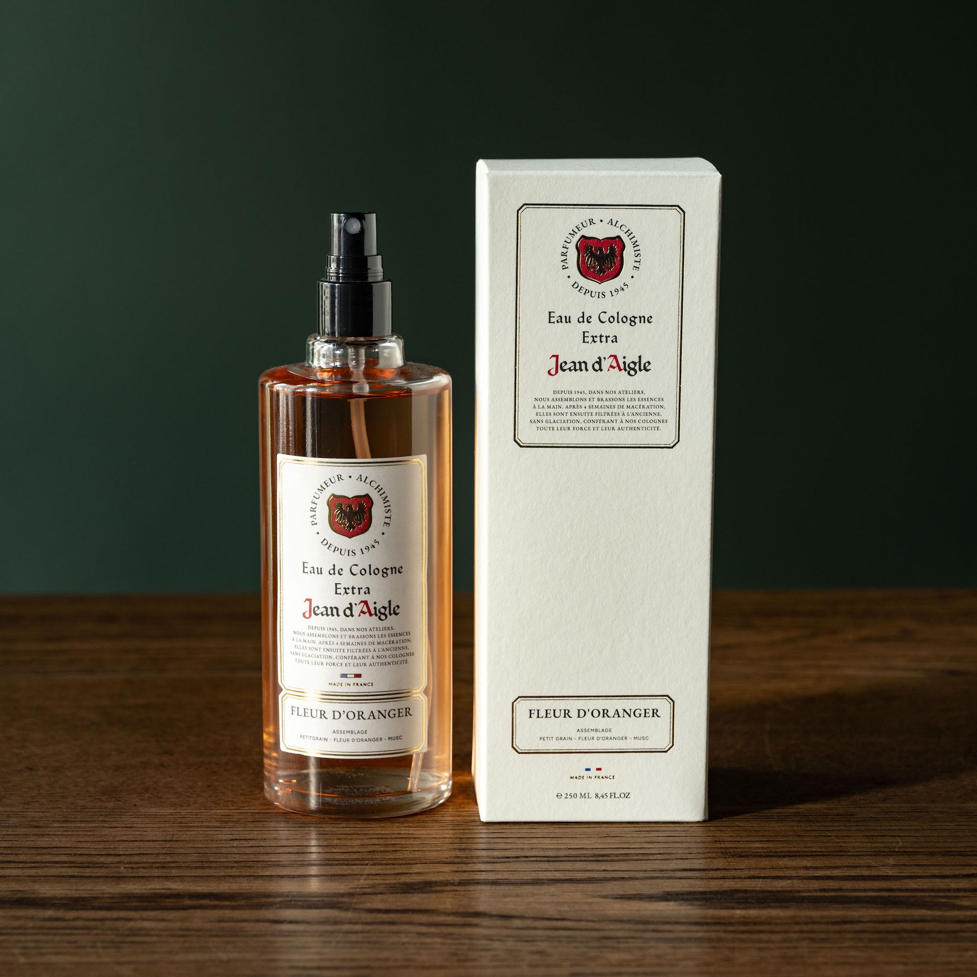 Bottle and box of Jean d'Aigle Fleur D'Oranger Eau de Cologne on a wooden surface with a dark background
