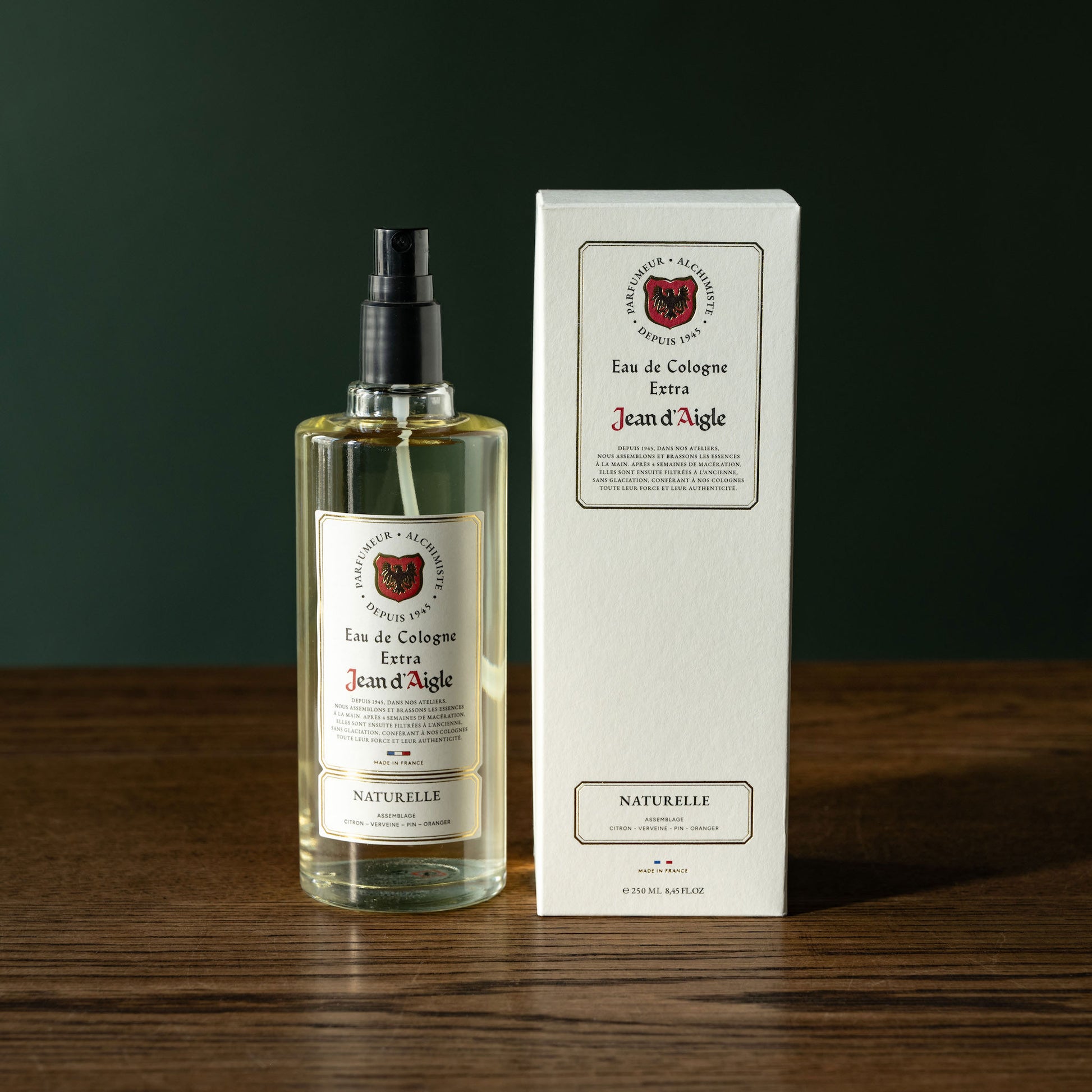 Bottle and box of Jean d'Aigle Naturelle Eau de Cologne on a wooden surface with a dark background