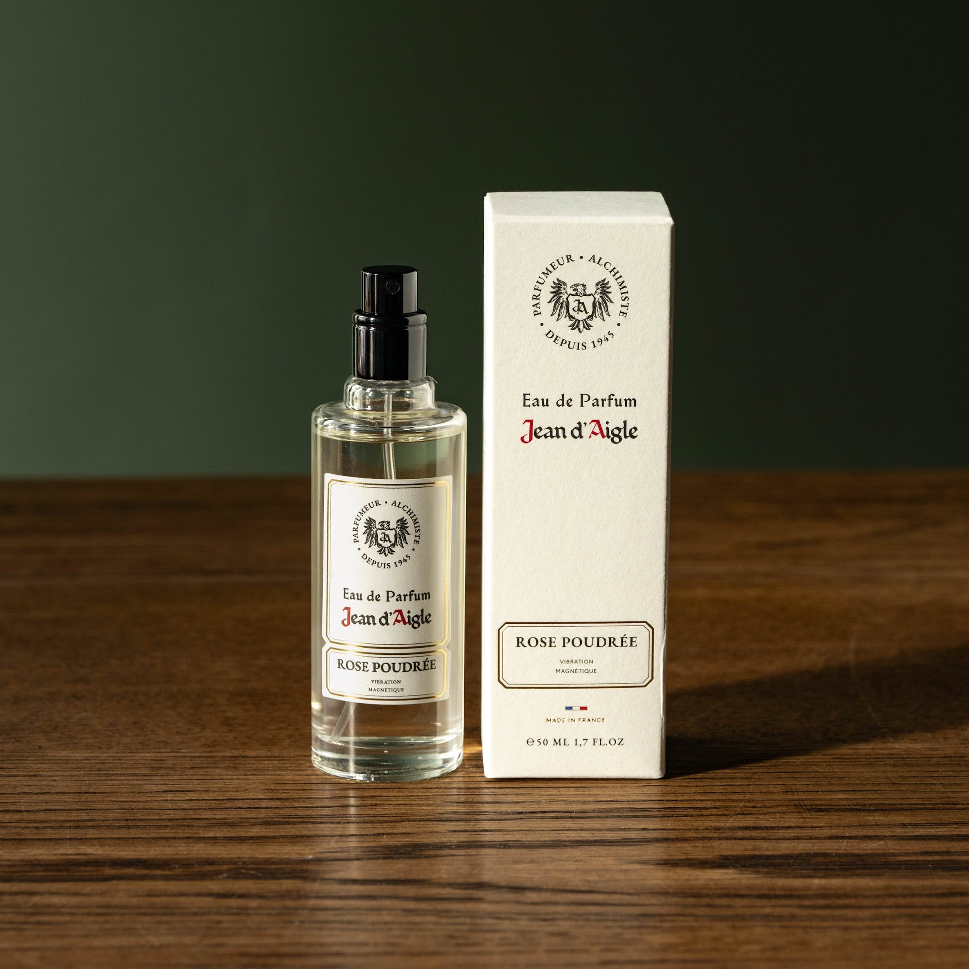 Jean d'Aigle Eau de Parfum Rose Poudree bottle and packaging on a wooden surface with a dark background