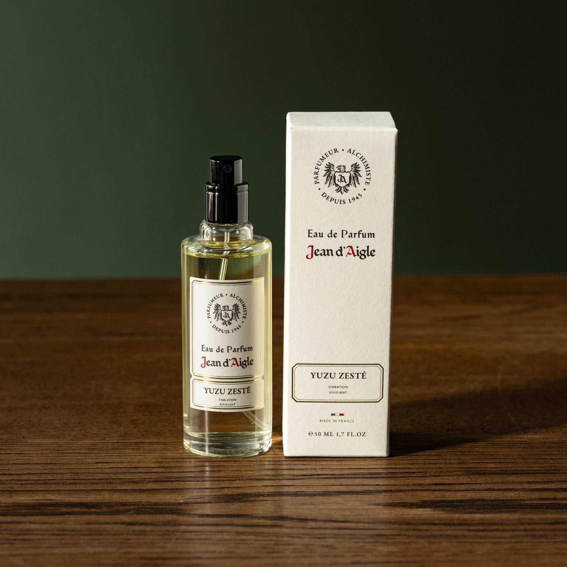 Jean d'Aigle Eau de Parfum Yuzu Zeste bottle and packaging on a wooden surface with a dark background