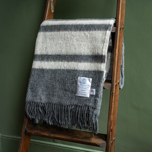 John Atkinson Winston grey and off white striped wool fringed blanket on a wooden ladder against a green wall.
