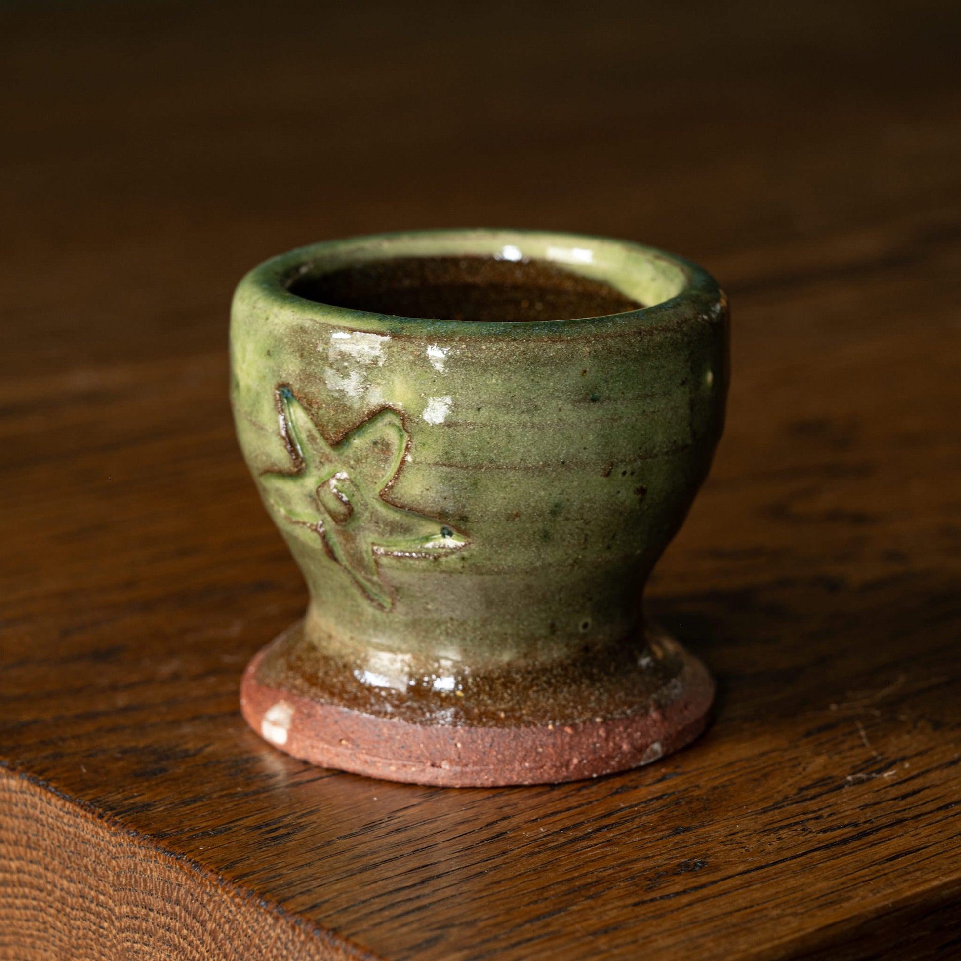 Joshua Williams green earthenware egg cup with a floral design on a wooden surface