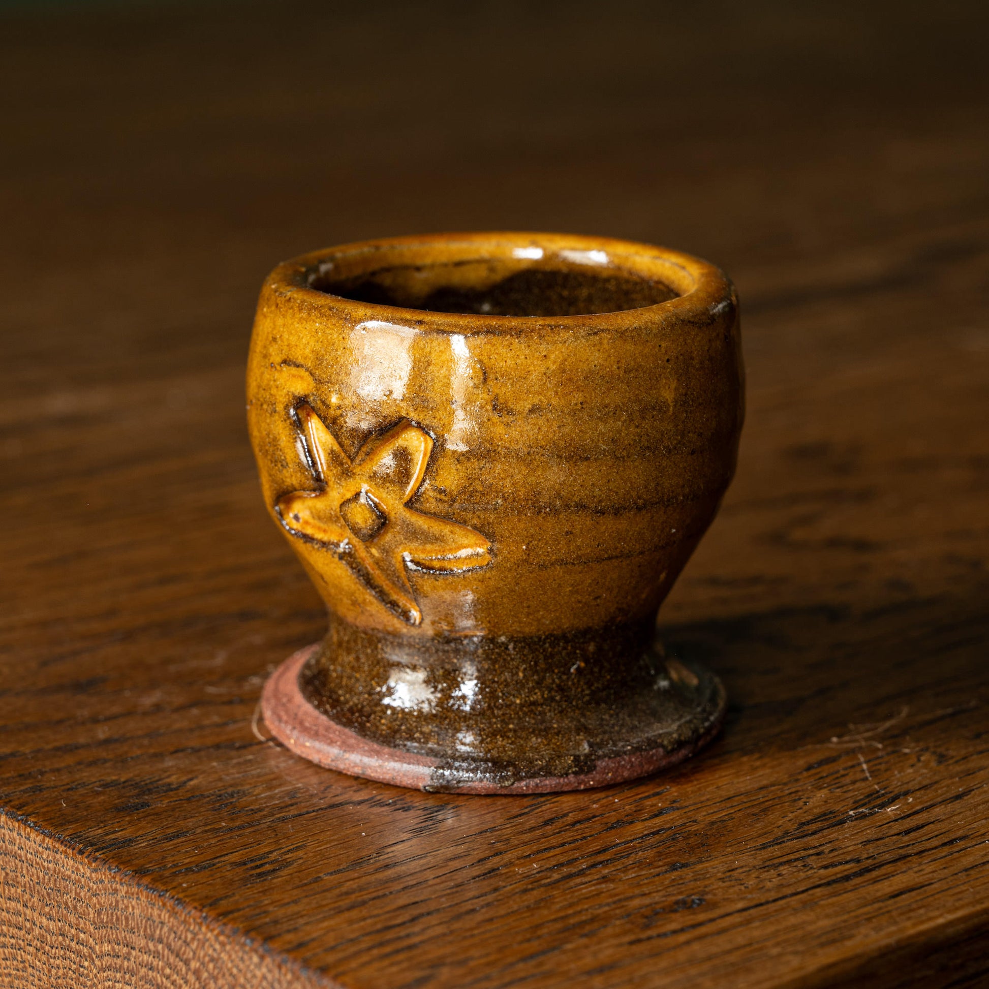 Joshua Williams ochre earthenware egg cup with floral design on a wooden surface