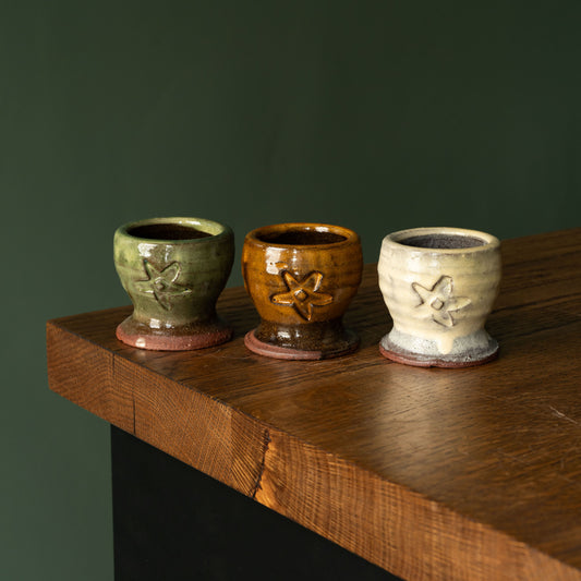 Joshua Williams Earthenware egg cups in assorted glazes on a wooden shelf