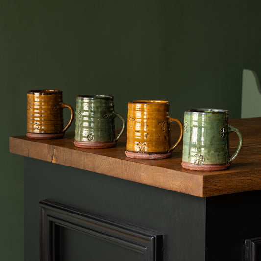 Four Joshua Williams earthenware mugs in different colorus on a wooden shelf 