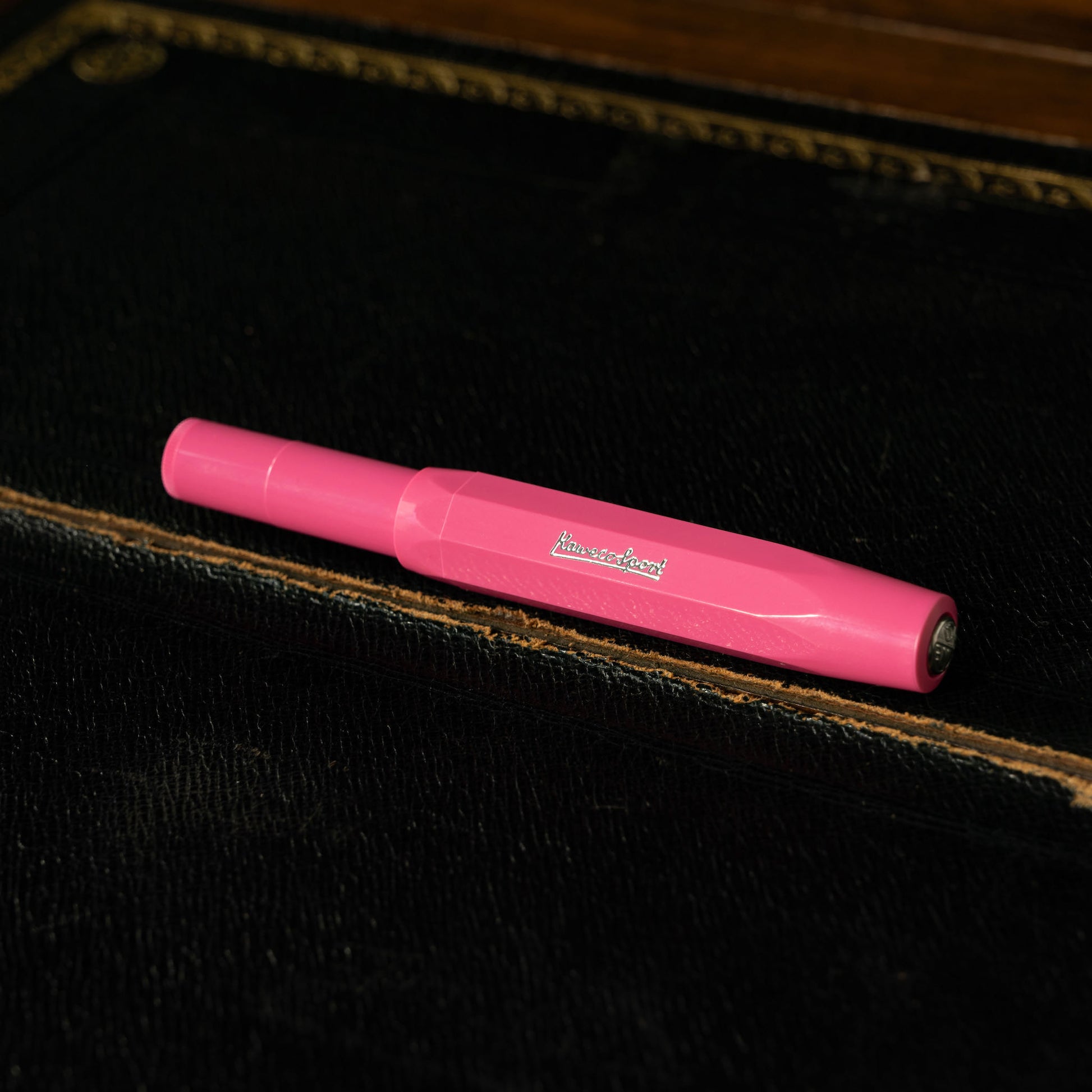 Kaweco Skyline Sport Pink Rollerball Pen with a visible brand logo on a dark leather writing desk surface