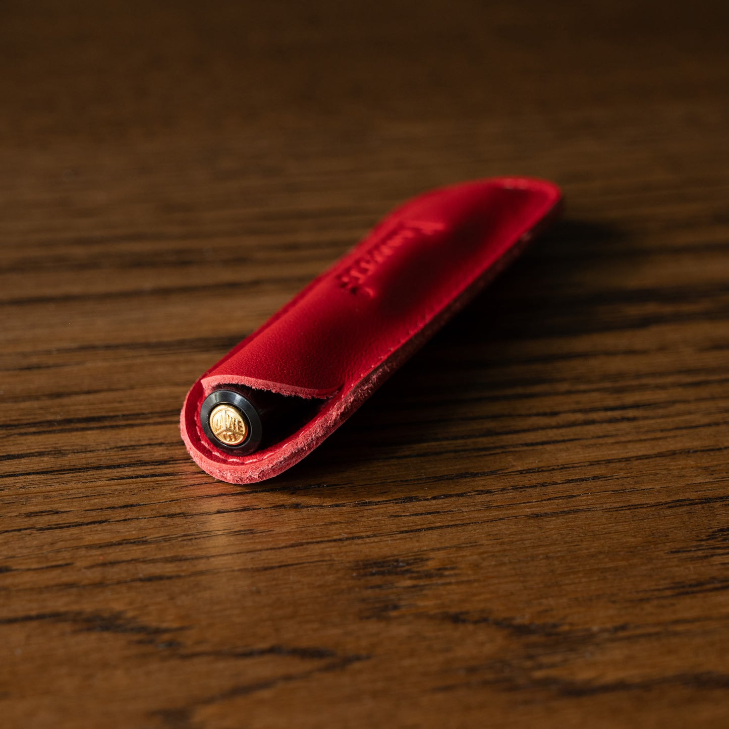 Kaweco red leather pen pouch with a black pen inside on a wooden surface