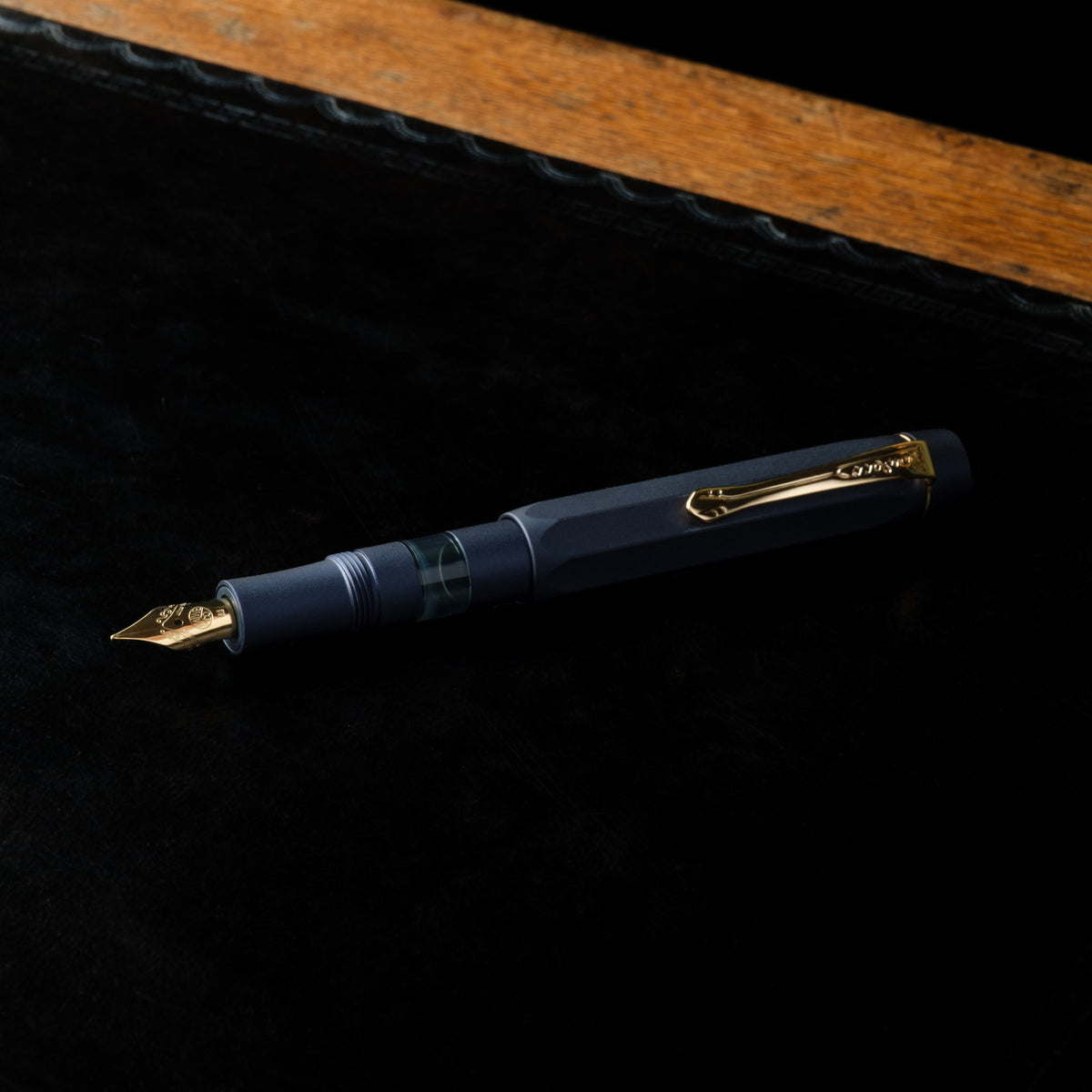 Kaweco Piston Sport AL Fountain Pen in  navy blue with gold-tone metal accents, including the nib, clip, and trim, resting on a black textured surface.