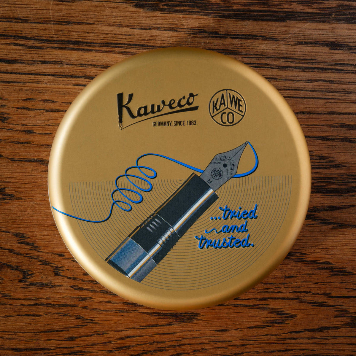 Presentation Lid of the Kaweco Piston Sport AL Starter Pack, featuring a blue ink coil and nib illustration, placed on a dark wood background.
