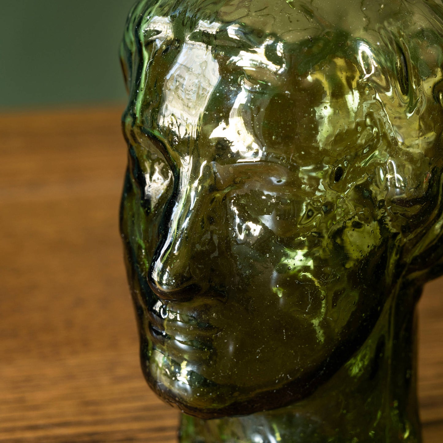Moulded face detail of La Soufflerie Roma Droit vase in dark green recycled glass. 