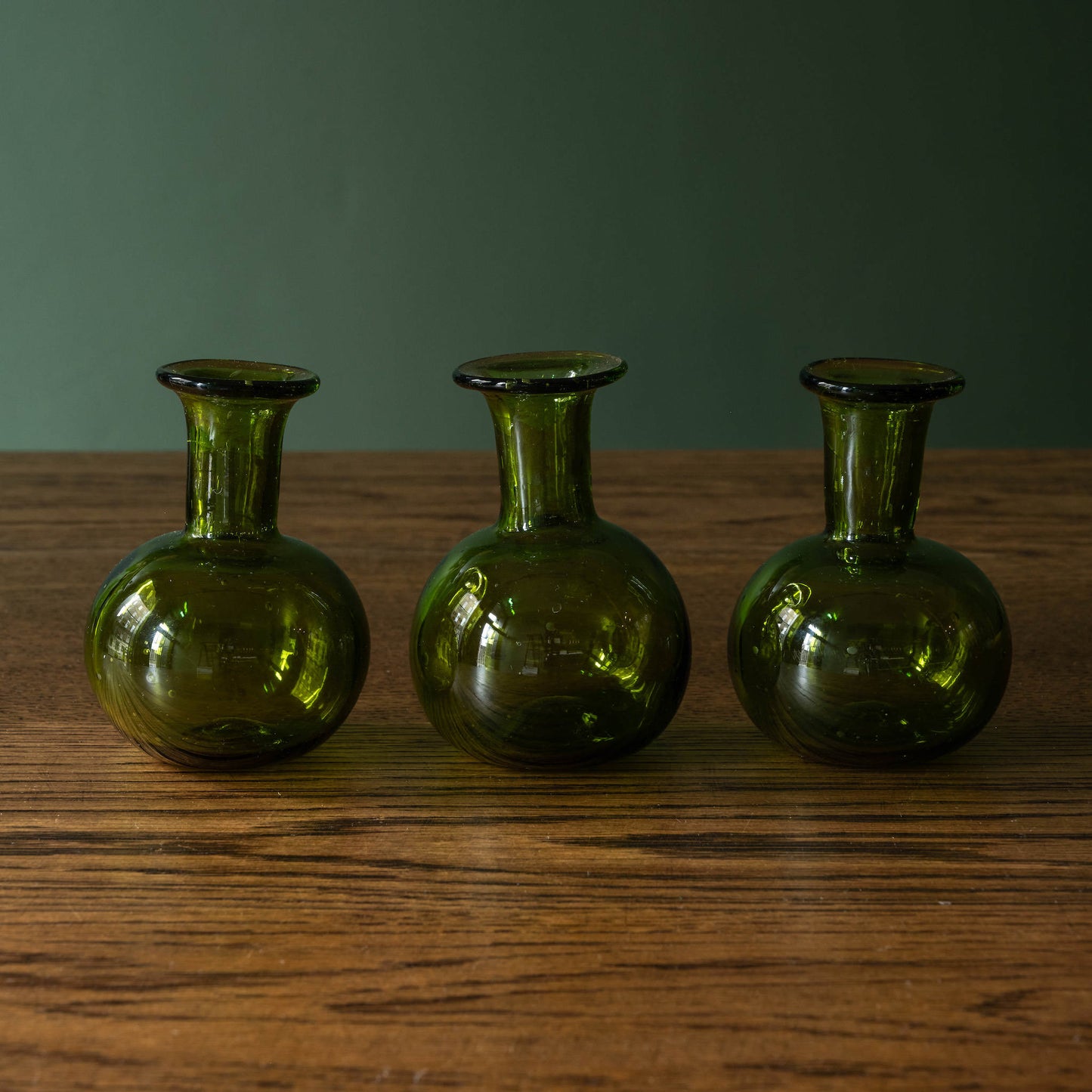 Three La Soufflerie small green glass bud vases  on a wooden surface 